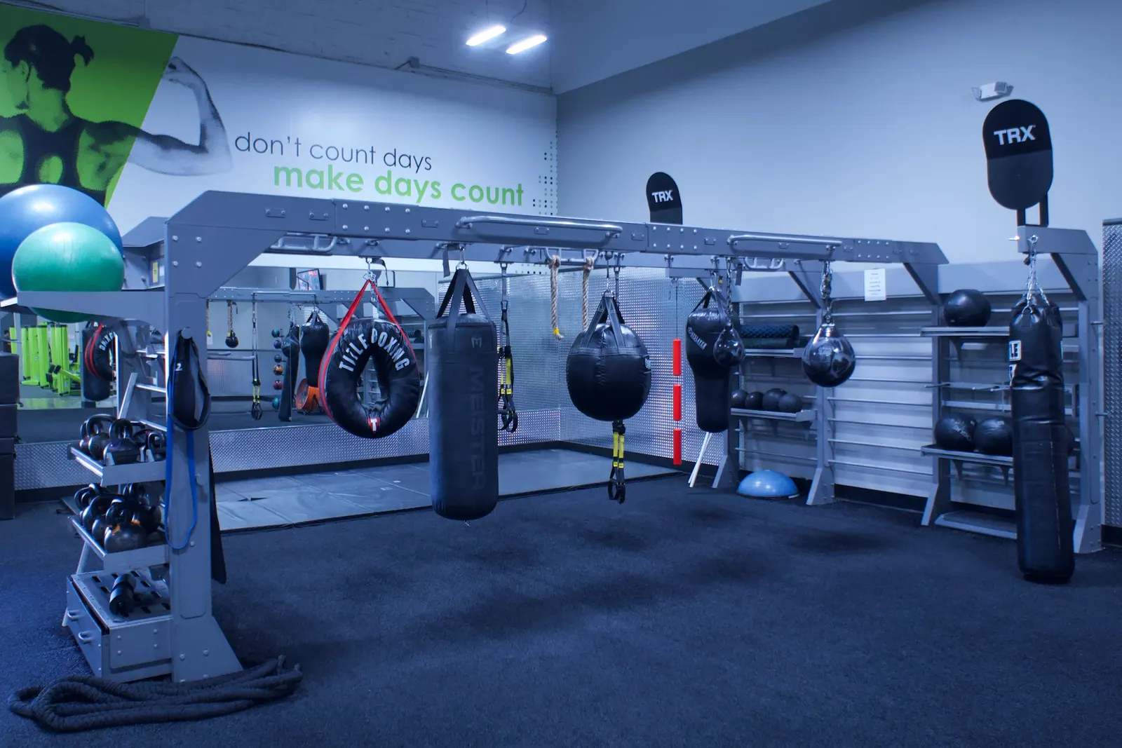 A line of heavy bags hanging from a rig, with ropes and weighted balls stored underneath.