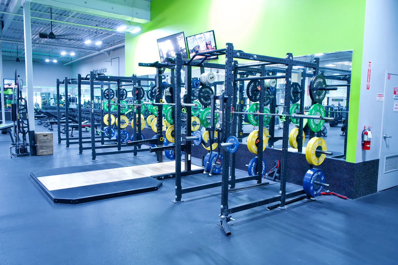 Power racks loaded with bumper plates against a bright green wall, with a lifting platform in front.