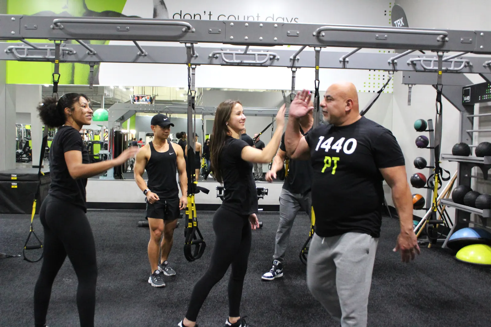 Three people at the suspension rig on the turf, one of them reaching up for a high five.