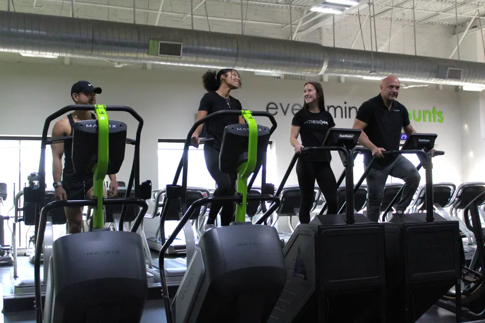 Four people on stair climbers, two of them laughing with each other.
