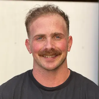Alex Metzler smiling, in a black T-shirt, against a white wall.