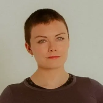 McKenzie in a dark long-sleeved top, against a white wall.